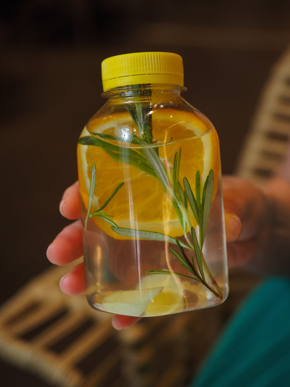 Hand holding a bottle of lemon and rosemary infused water