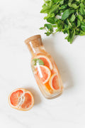 Cork-topped glass bottle filled with pink grapefruit slices and mint leaves