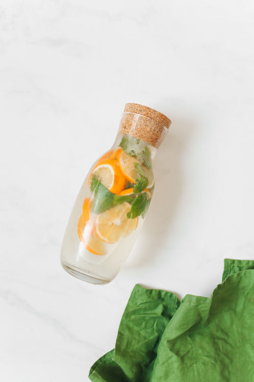 Cork-topped glass bottle of water infused with orange slices and mint